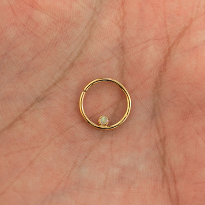 A model's hand holding a 14 karat yellow gold opal Pierced Raised Gemstone Septum