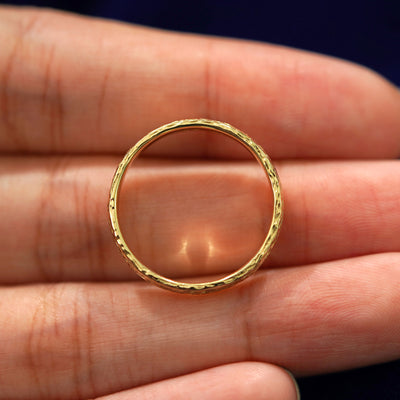 A yellow gold Raw Band in a model's hand showing the thickness of the band