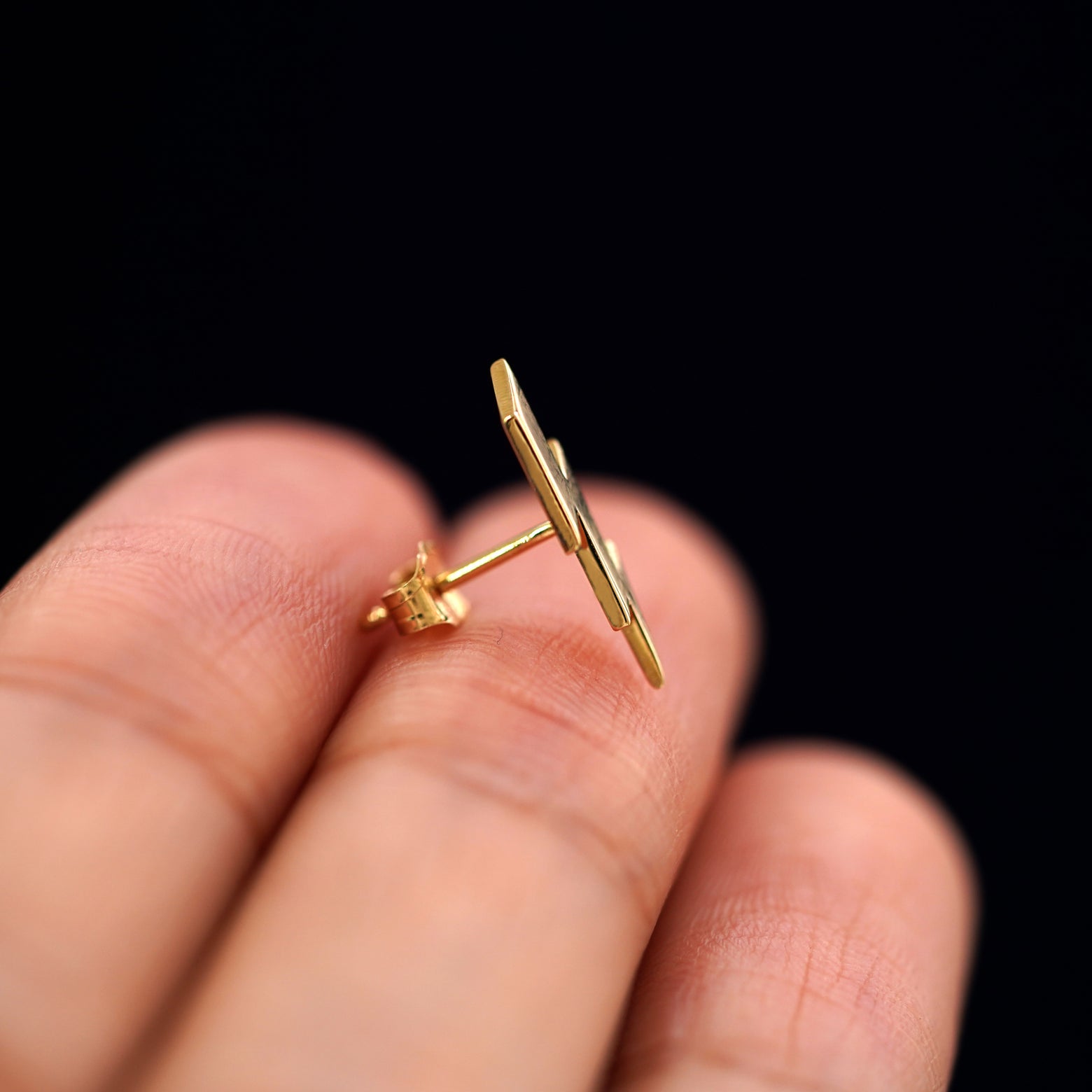 A 14k gold Lightning Bolt Earring sitting sideways on a model's fingertips to show detail