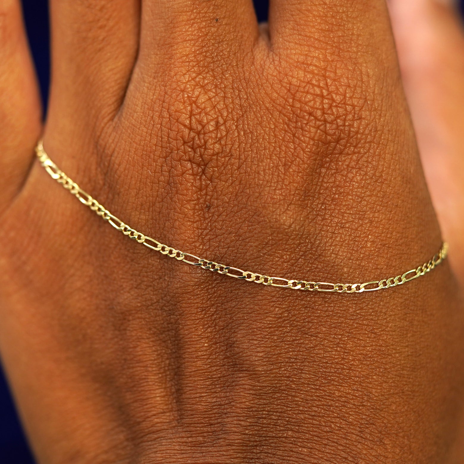 A solid gold Figaro Bracelet resting on the back of a model's hand