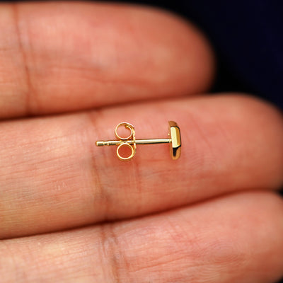 A 14k gold Hexagon Earring sitting sideways on a model's fingertips to show detail