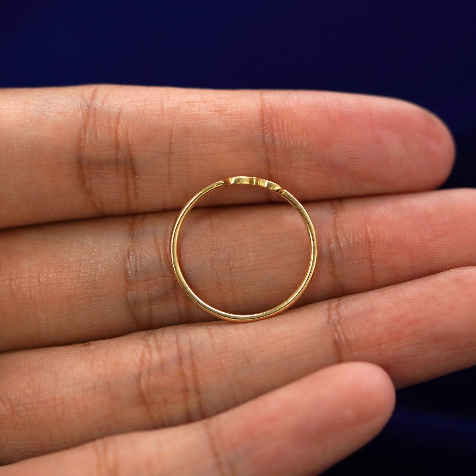 A yellow gold Infinity Ring in a model's hand showing the thickness of the band