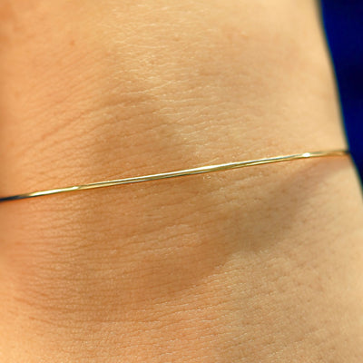 Close up view of a model's wrist wearing a solid gold Line Bangle Bracelet