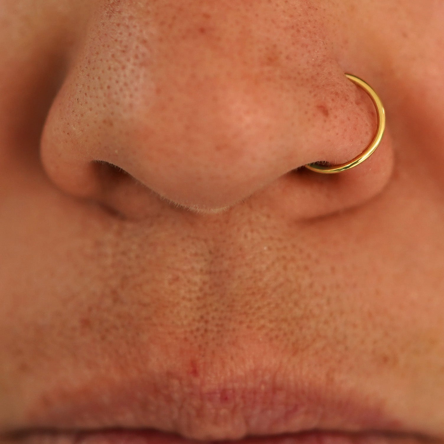 Close up view of a model's nose wearing a 14k yellow gold Nose Ring Hoop