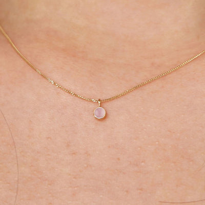 Close up view of a model's neck wearing a solid 14k yellow gold Rose Quartz necklace