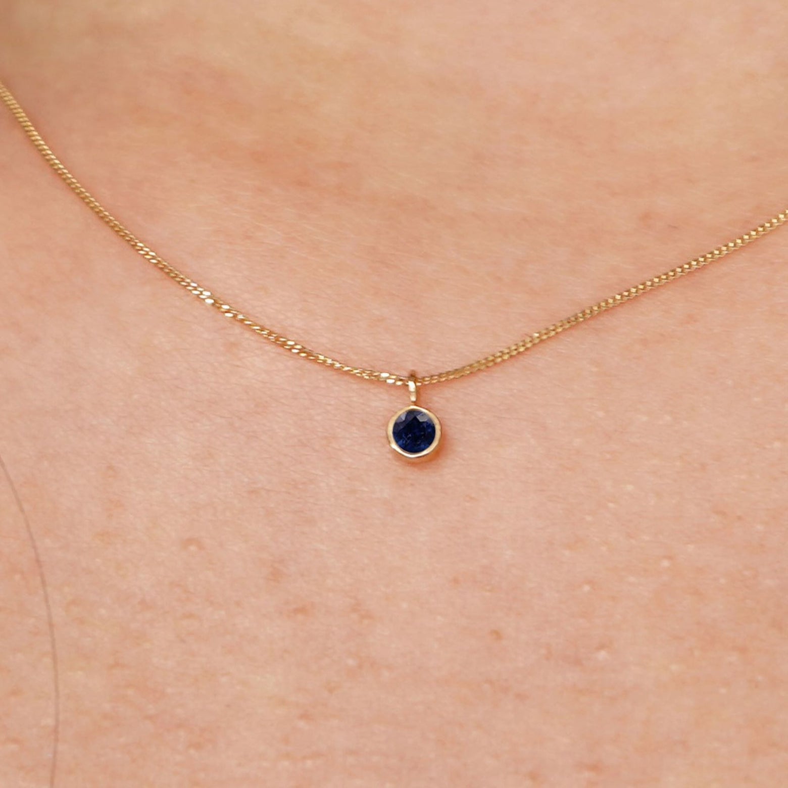 Close up view of a model's neck wearing a solid 14k yellow gold Sapphire necklace