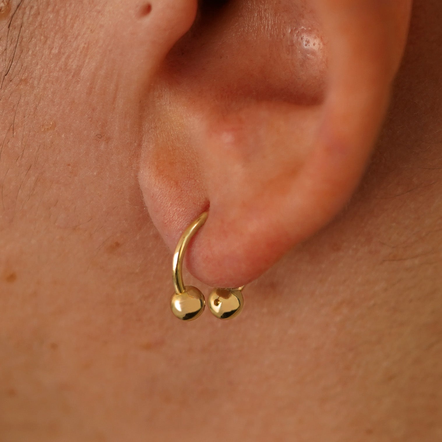 Close up view of a model's ear wearing a 14k yellow gold Small Horseshoe  through a lobe piercing