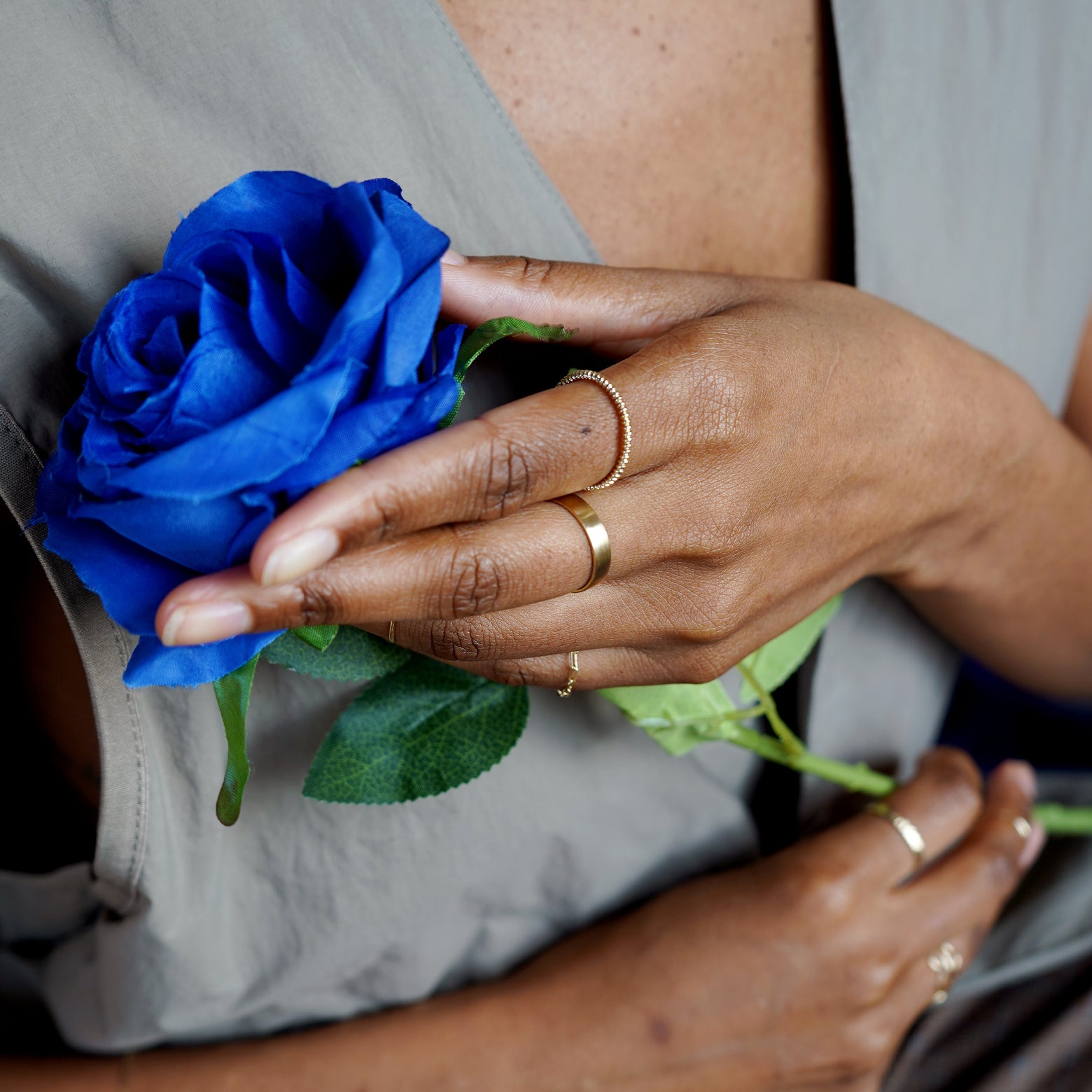 A model cradling a blue rose wearing a Rope Ring, an Industrial Mirror Band, and a Butch Chain Ring