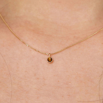 Close up view of a model's neck wearing a solid 14k yellow gold Tiger Eye necklace