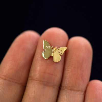 A yellow gold Butterfly Earring laying facedown on a model's fingers to show the underside view
