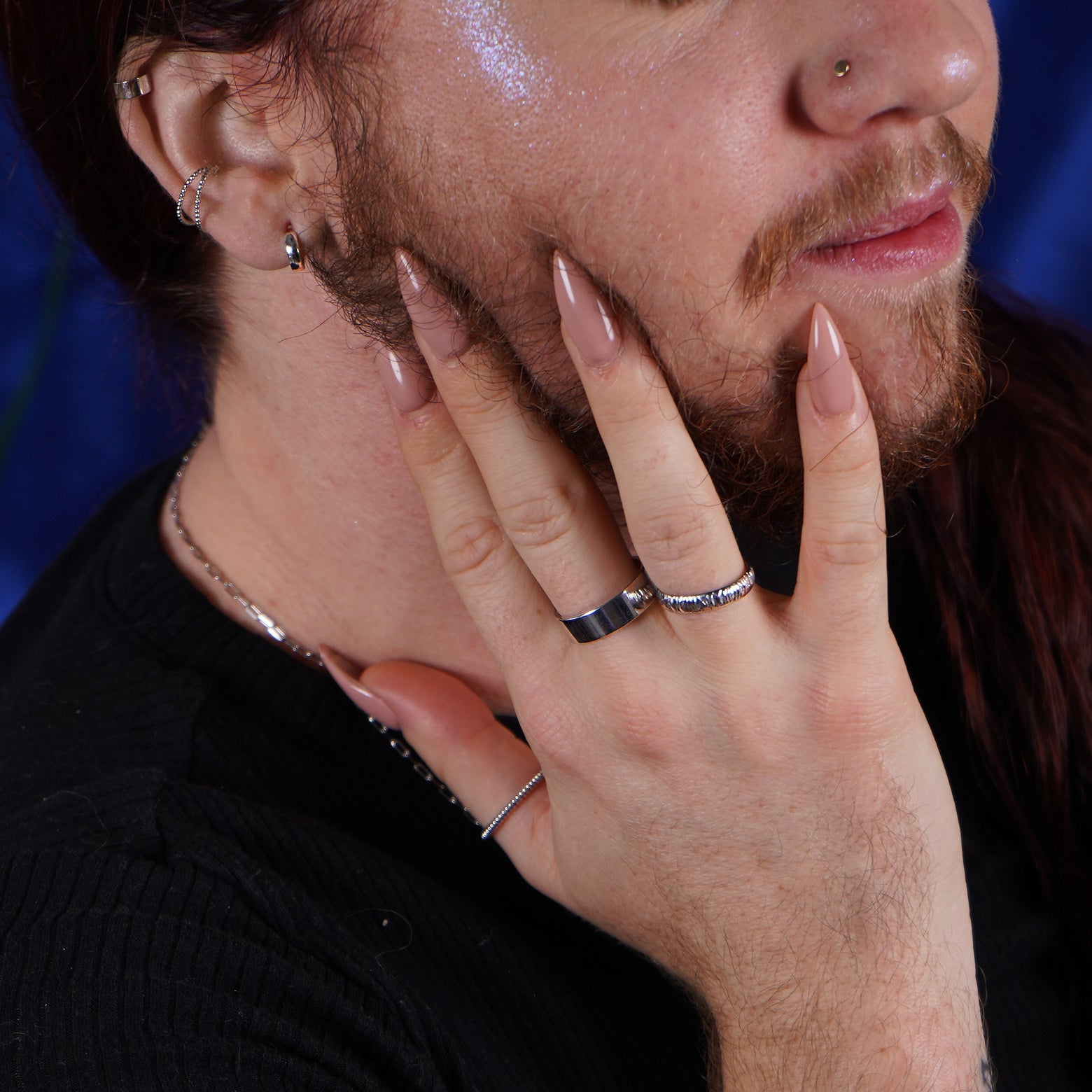 A model with pointed nails wearing a white gold rope ring, an industrial mirror band, and an industrial wood band