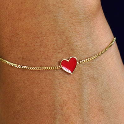 Close up view of a model's wrist wearing a yellow gold red enamel heart bracelet