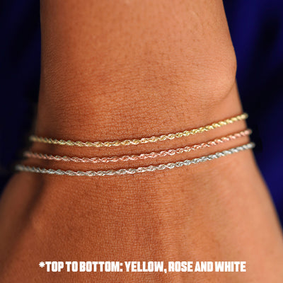 Close up view of a model's wrist wearing a three  versions of the Rope Anklet in yellow, rose, and white gold