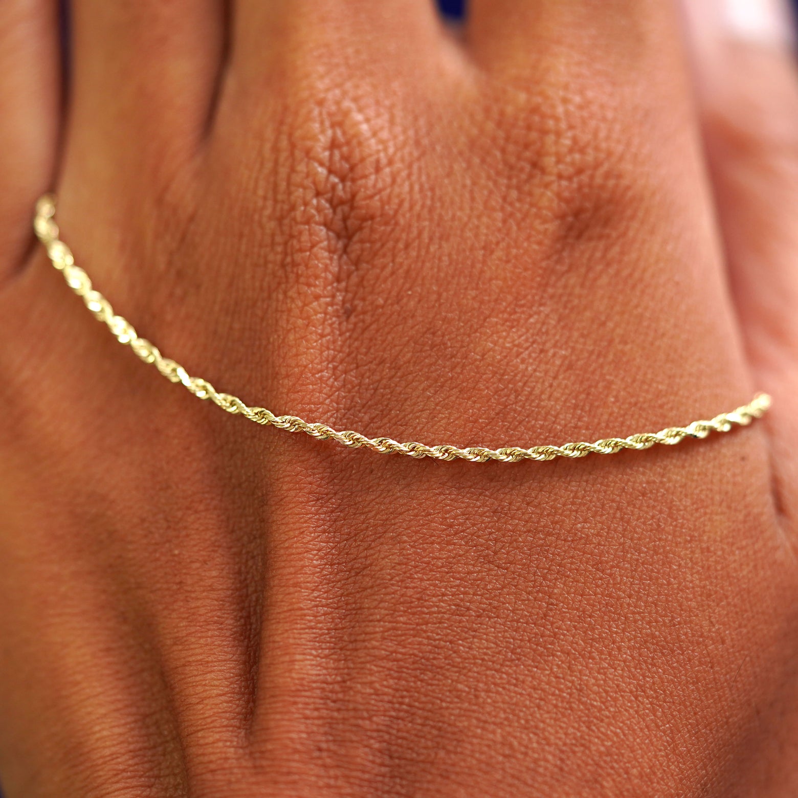 A solid gold Rope Anklet resting on the back of a model's hand