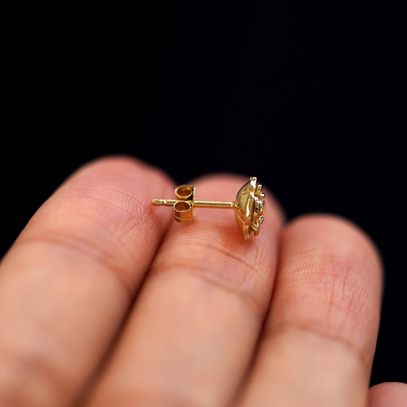 A 14k gold Rose Earring sitting sideways on a model's fingertips to show detail