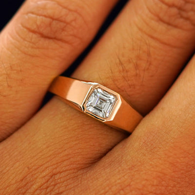 Close up view of a model's fingers wearing a rose gold white Asscher Moissanite Signet Ring