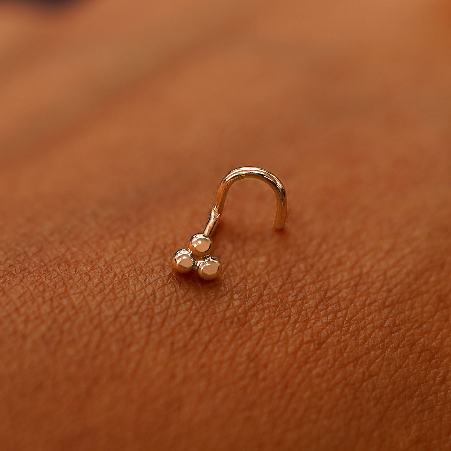 A rose gold Ball Trio Nose Stud laying on the back of a model's hand