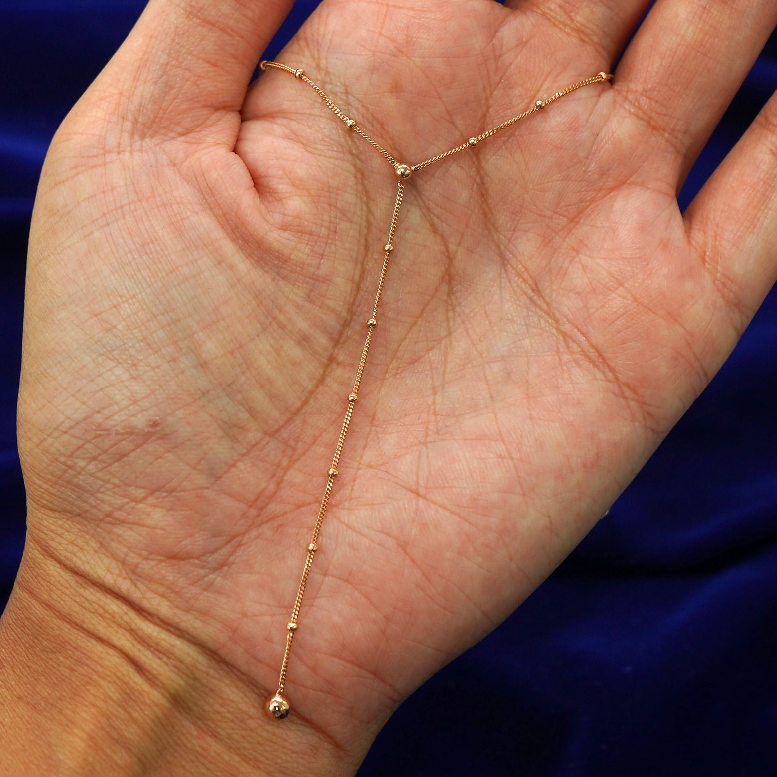 A rose gold Beaded Essential Lariat Necklace draped on a model's palm