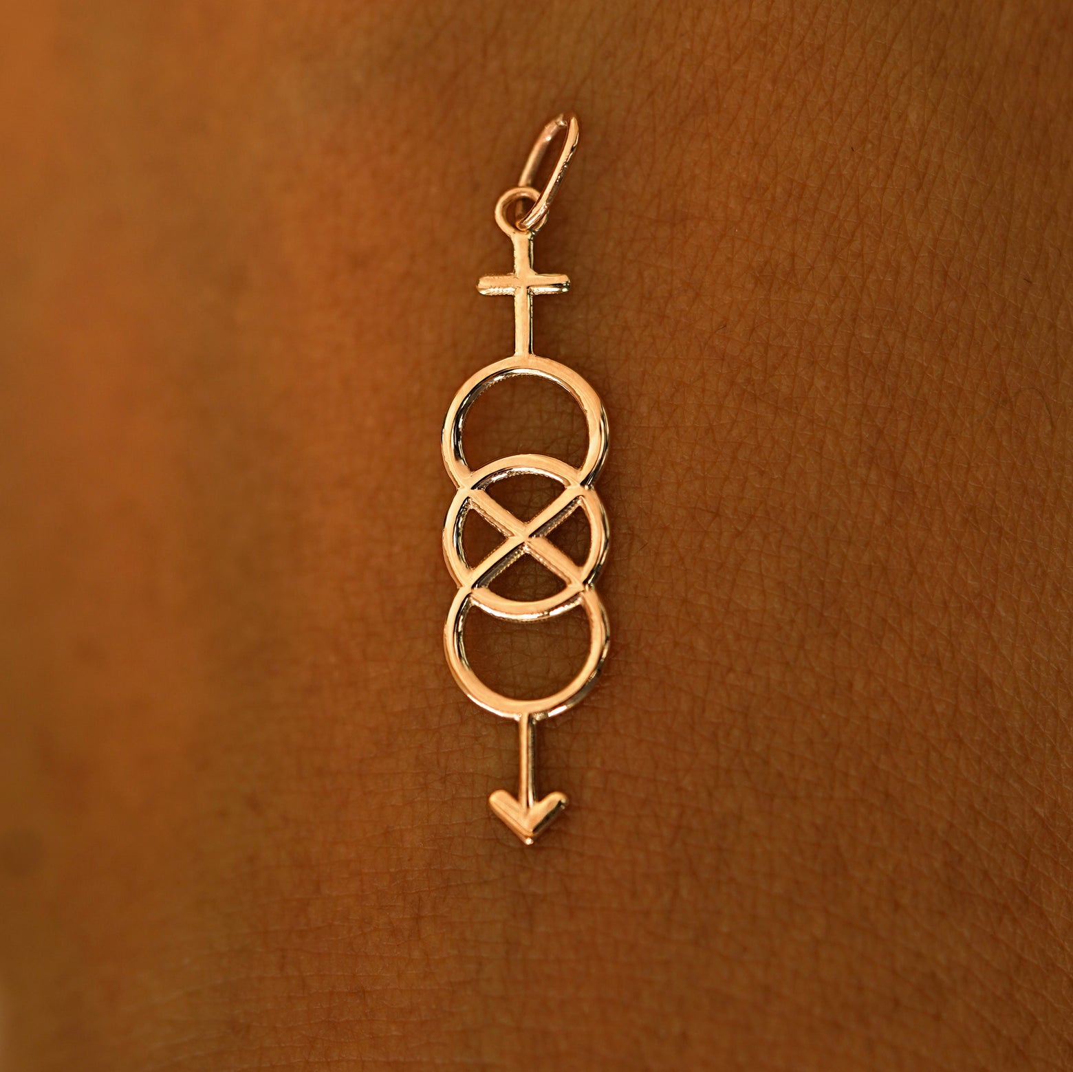 A solid 14k rose gold Bisexual Symbol Charm resting on the back of a model's hand