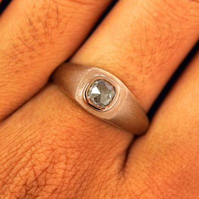 Close up view of a model's fingers wearing a 14k rose gold Cushion Salt and Pepper Diamond Signet Ring