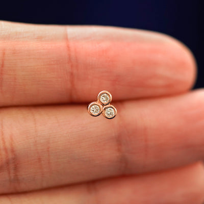 A hand holding a 14k rose gold Diamond Trio stud Flatback Piercing in between their fingers