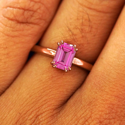 Close up view of a model's fingers wearing a 14k rose gold Emerald Cut Pink Sapphire Ring