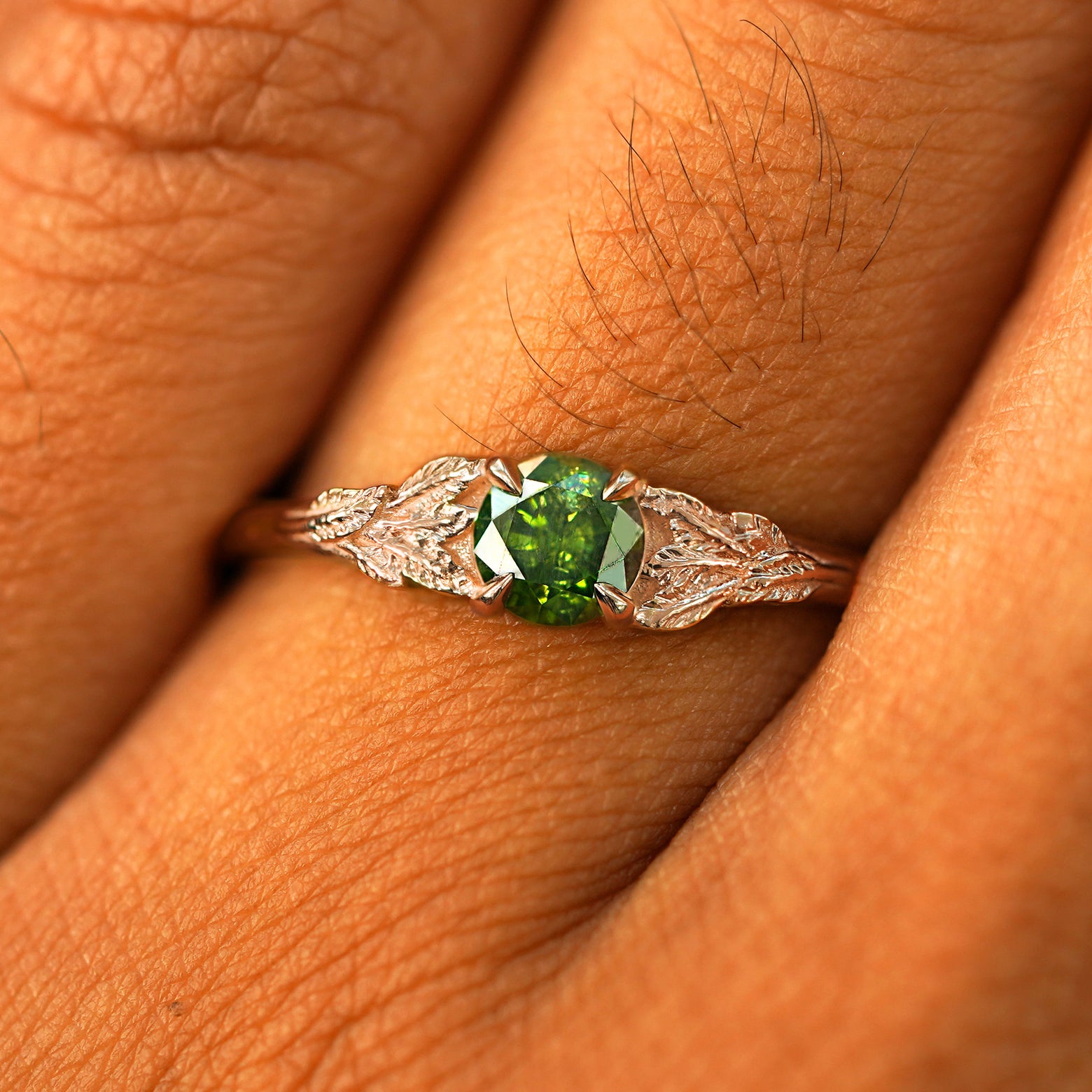 Close up view of a model's fingers wearing a 14k rose gold Green Diamond Leaves Ring