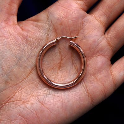 A solid 14k rose gold Large Tube Hoop Earring closed in a model's palm