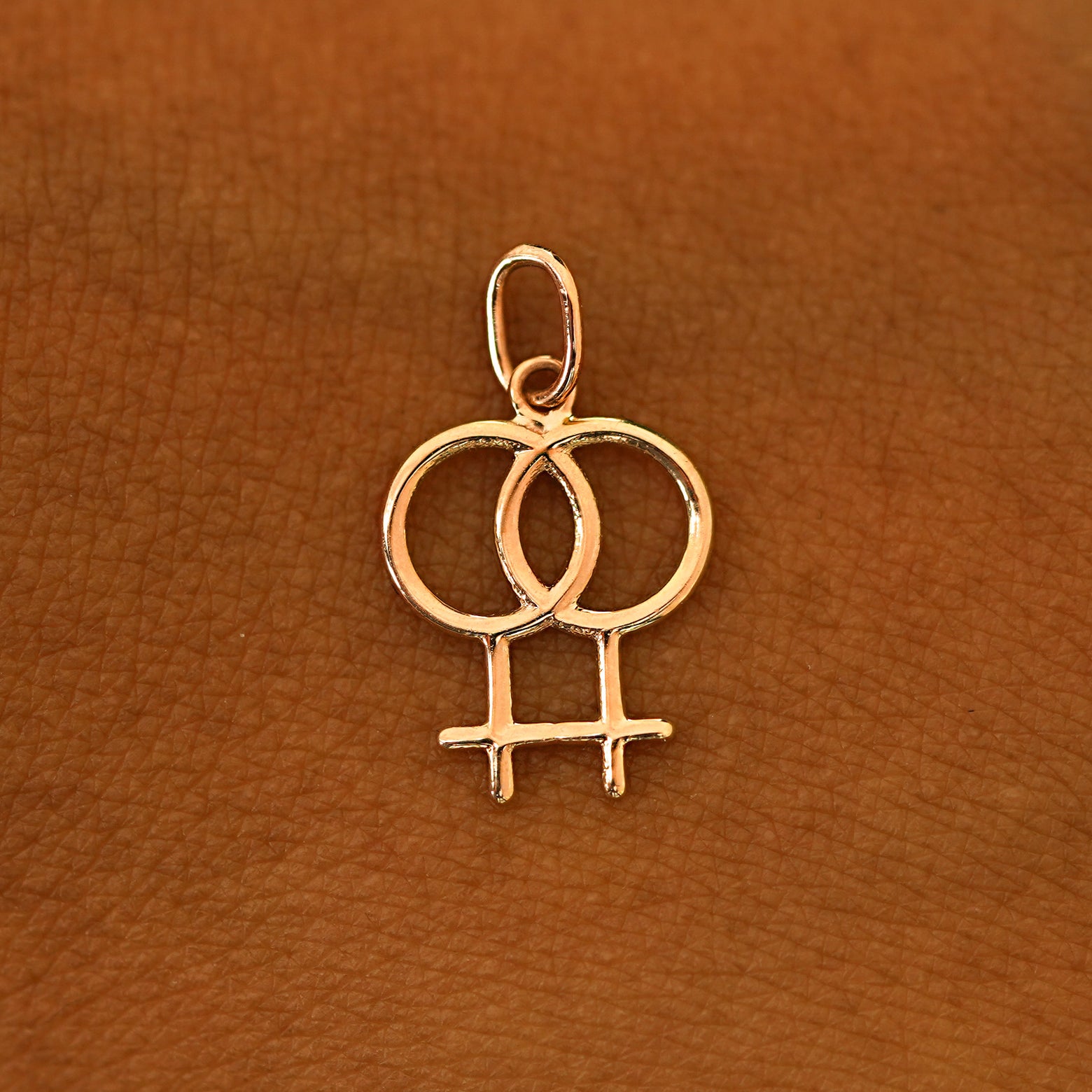 A solid 14k rose gold Lesbian Symbol Charm resting on the back of a model's hand