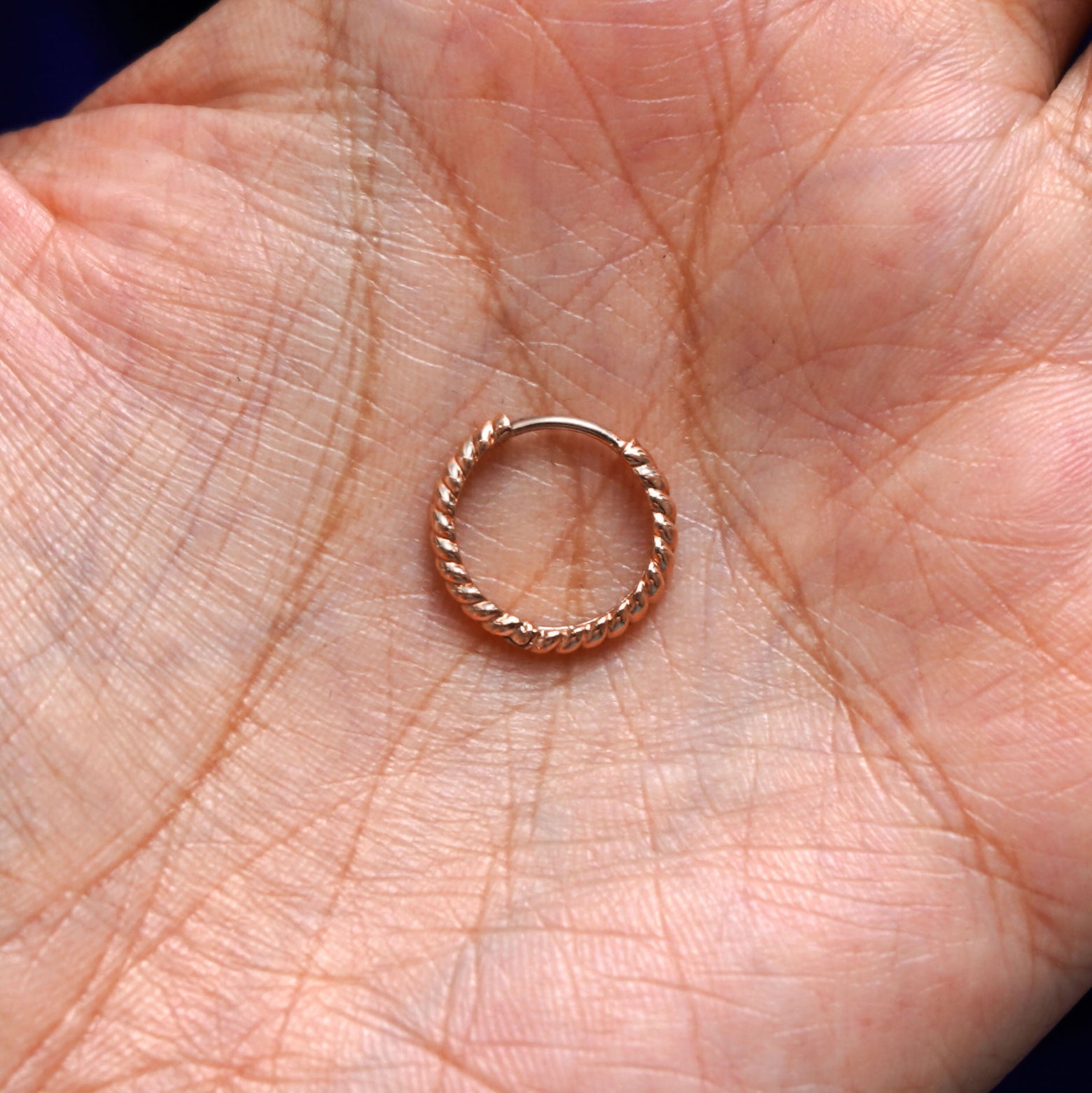 A solid 14k rose gold Medium Rope Huggie Hoop Earring closed in a model's palm