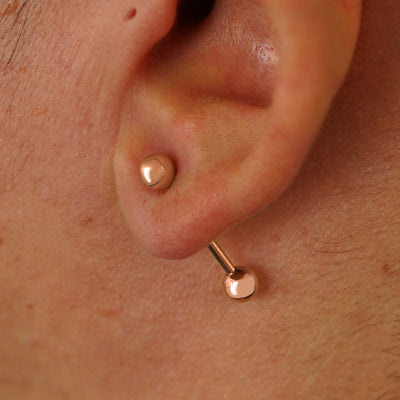 Close up view of a model's ear wearing a 14k rose gold Medium Straight Barbell through a lobe piercing