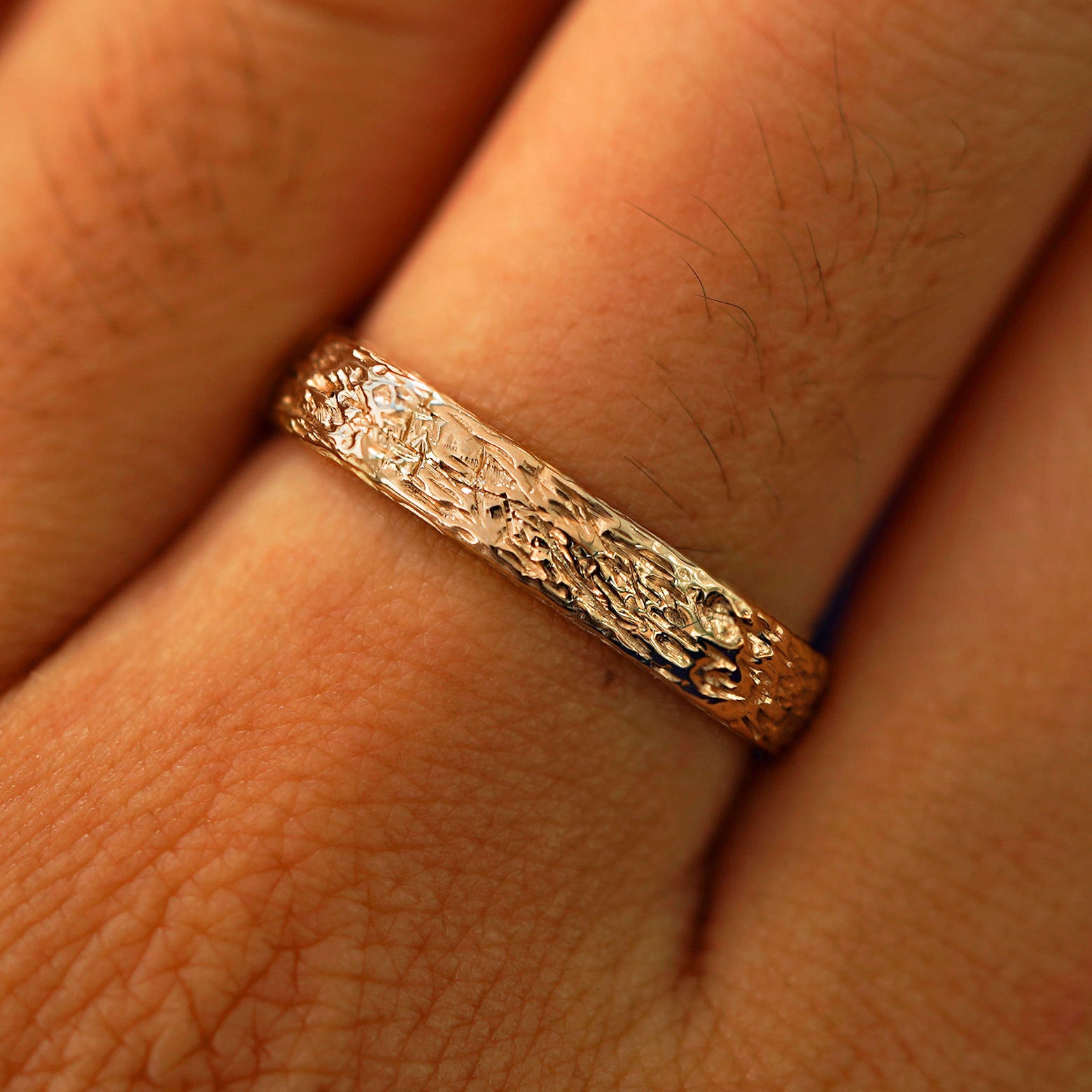 Close up view of a model's fingers wearing a 14k rose gold Raw Band