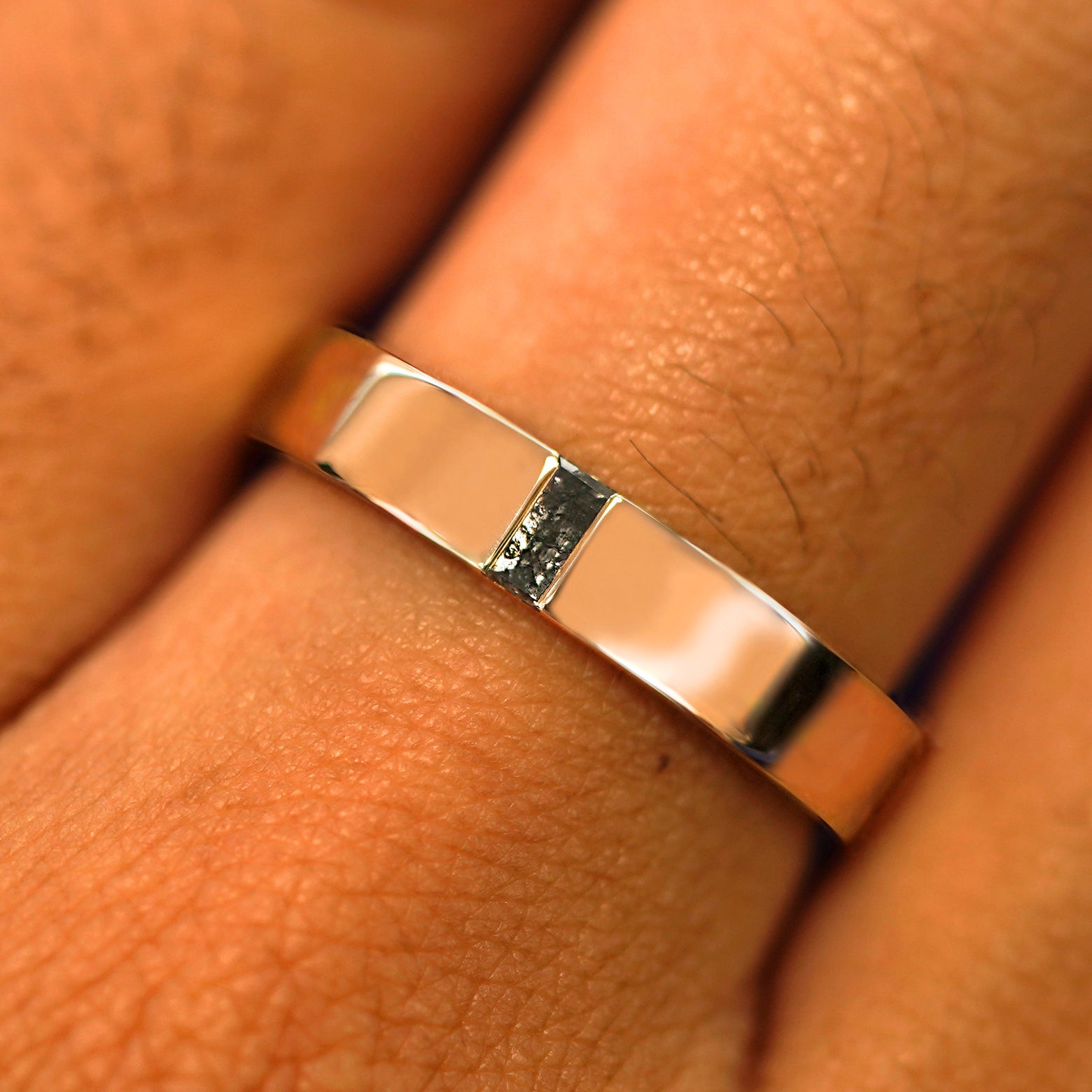 Close up view of a model's hand wearing a solid rose gold Salt and Pepper Baguette Diamond Band