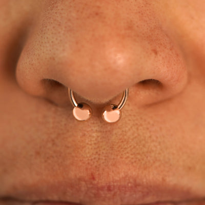 Close up view of a model's nose wearing a 14k rose gold Small Horseshoe in a septum piercing