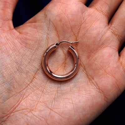 A solid 14k rose gold Small Tube Hoop Earring closed in a model's palm