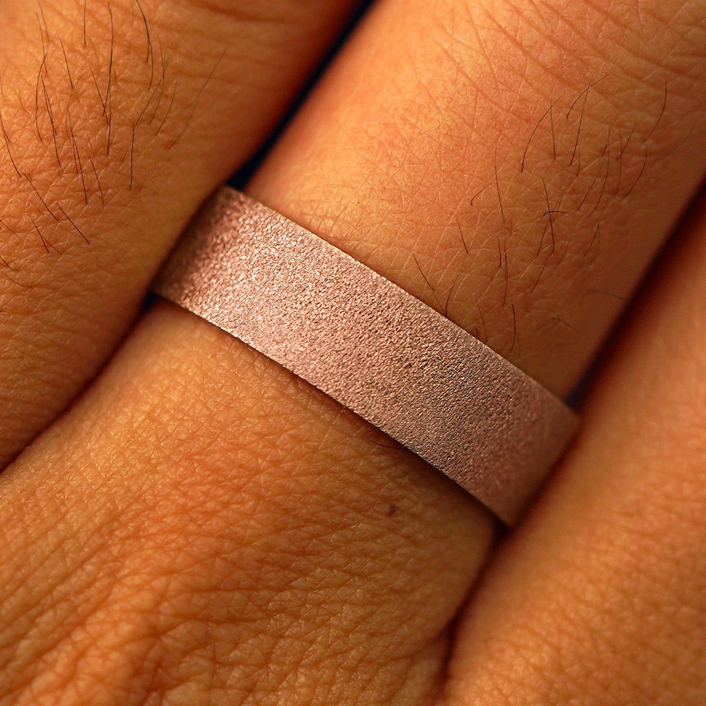 Close up view of a model's fingers wearing a 14k rose gold Industrial Stardust Band