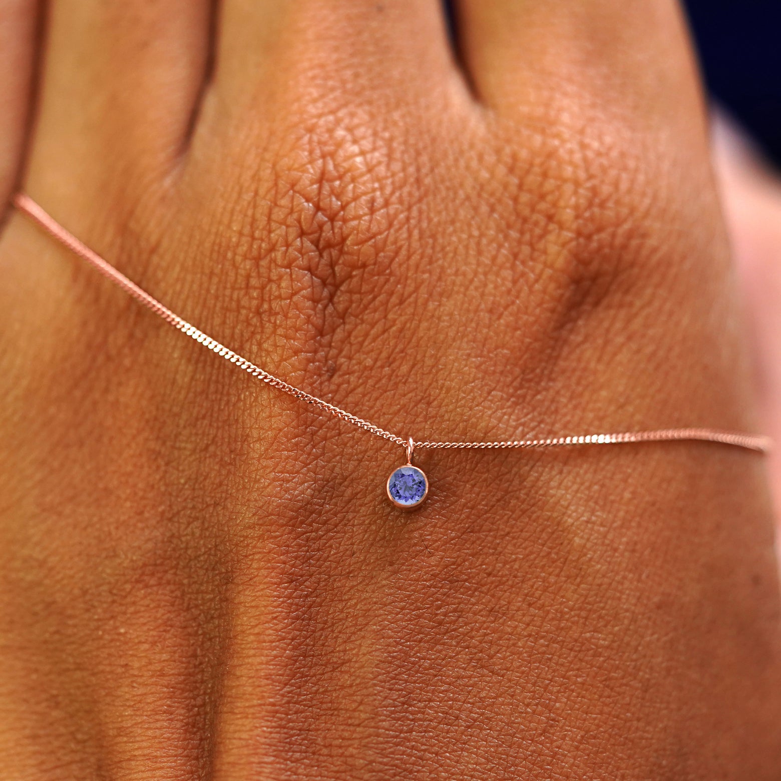 A solid rose gold Tanzanite Necklace draped across the back of a model's hand