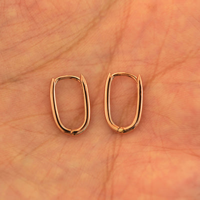 A pair of 14k rose gold Thin Oval Huggie Hoops resting in a model's palm