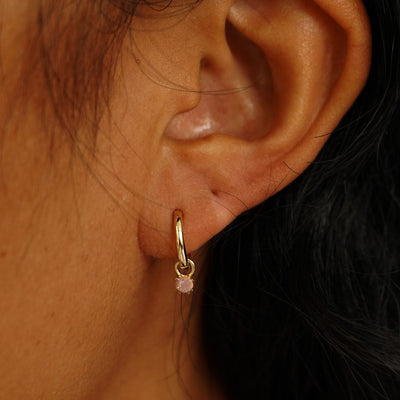 Close up view of a model's ear wearing a yellow gold Rose Quartz Charm on a Curvy Huggie Hoop