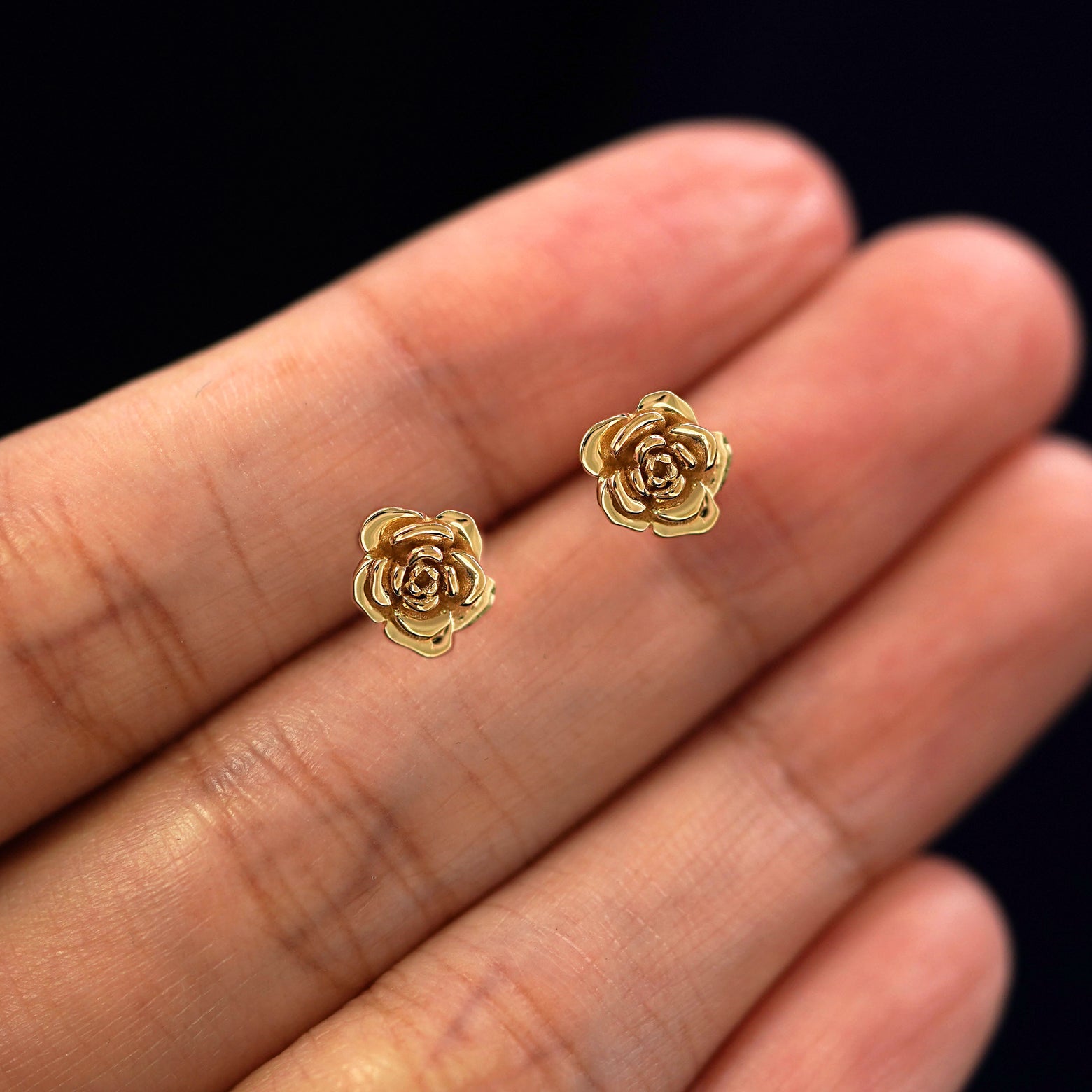 A model's hand holding a pair of recycled 14k gold Rose Earrings