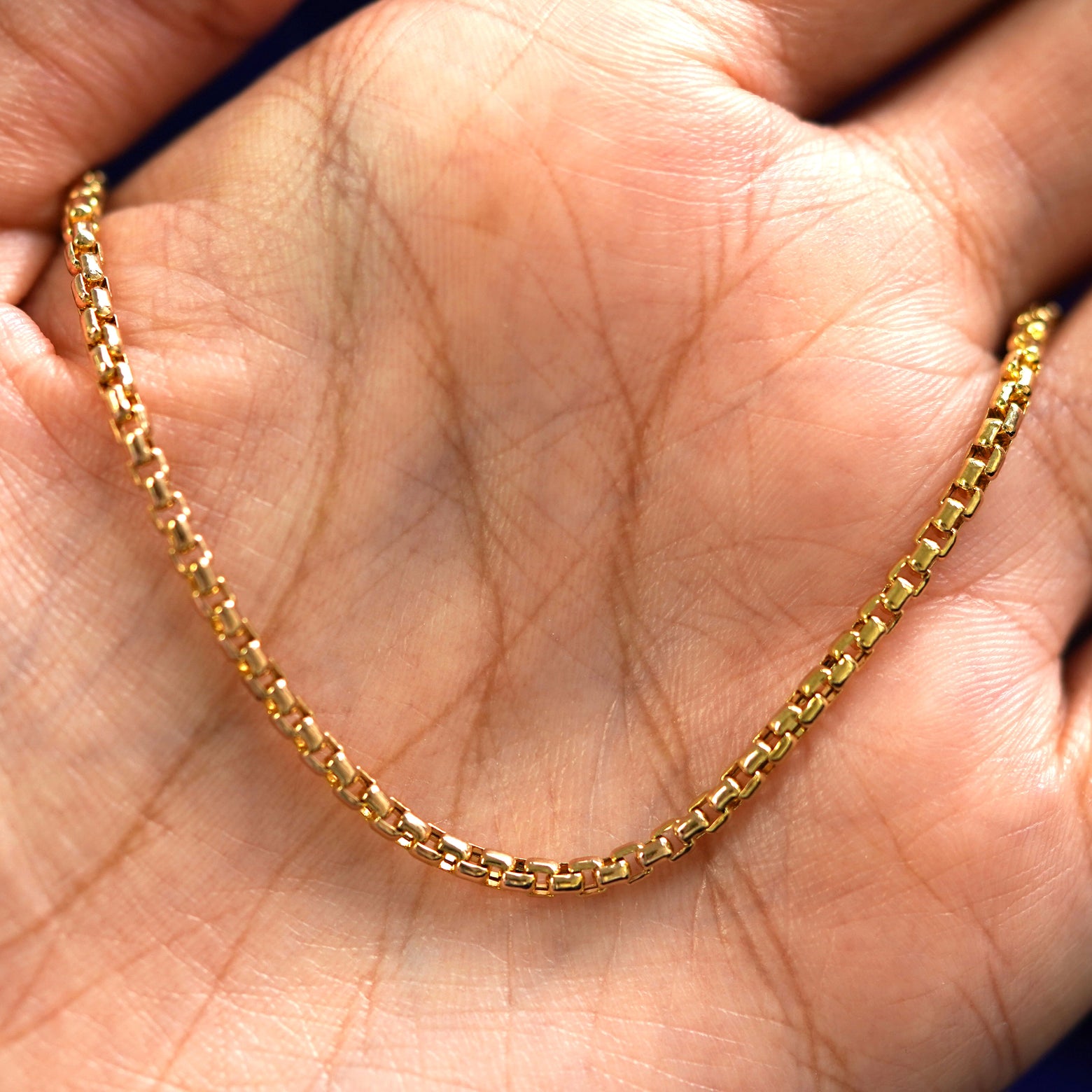 A yellow gold Round Box Bracelet draped on a model's palm