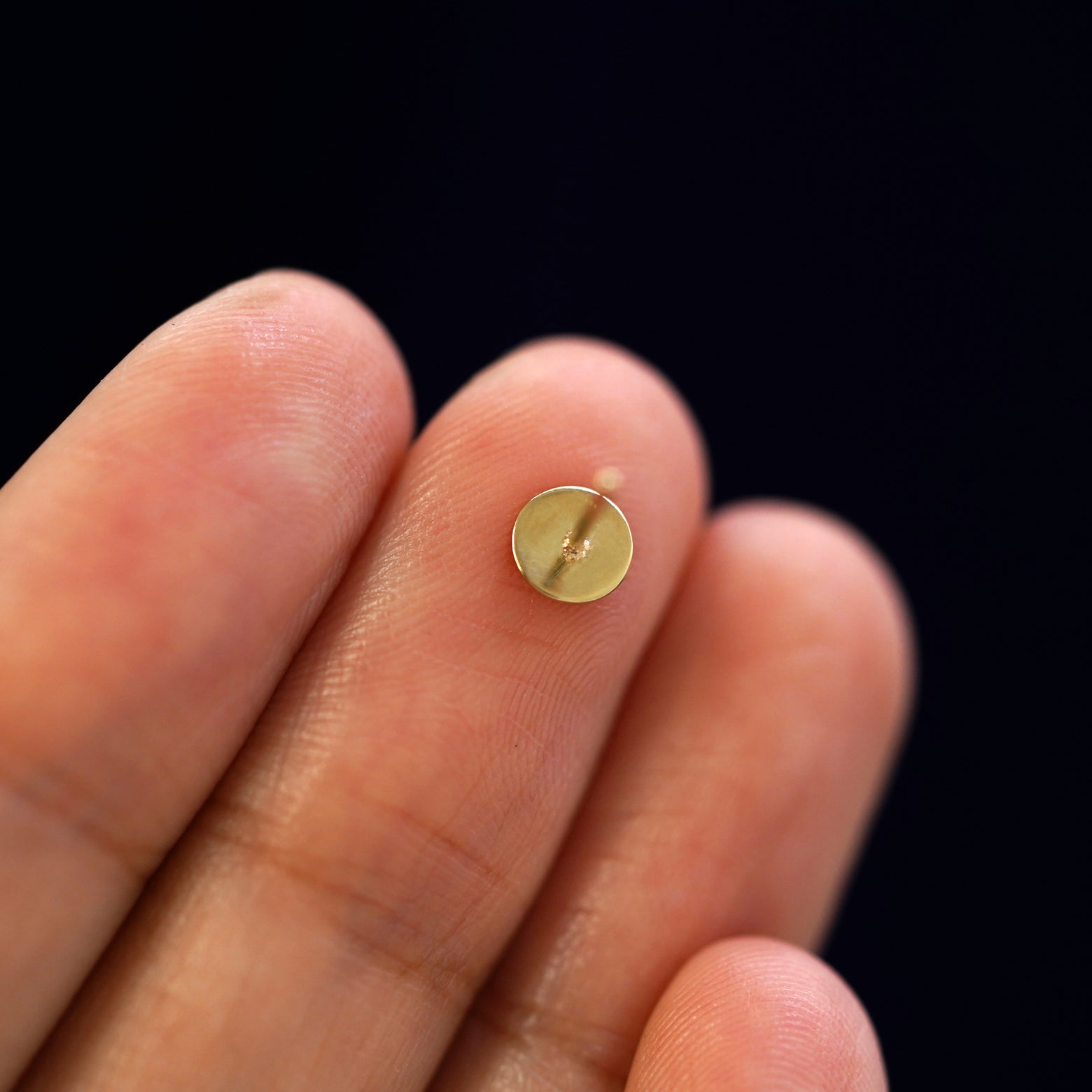 A yellow gold Screw Earring laying facedown on a model's fingers to show the underside view