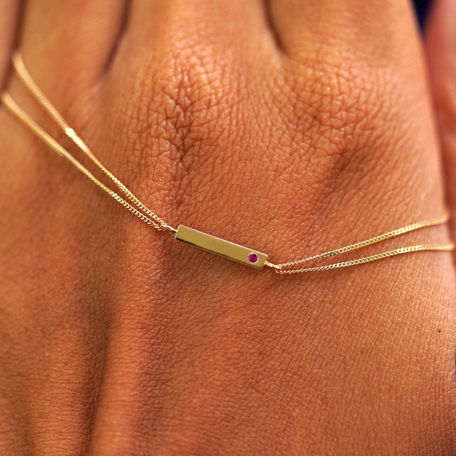 A solid gold ruby Gemstone Bar Bracelet resting on the back of a model's hand