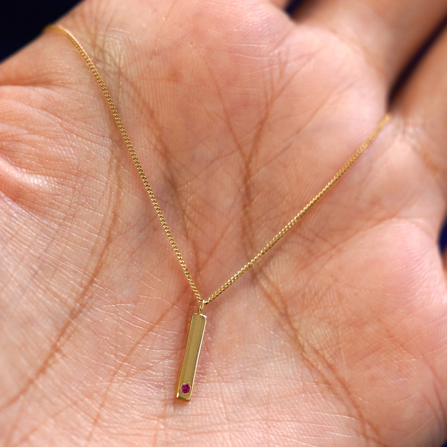 A yellow gold ruby Gemstone Bar Necklace draped on a model's palm