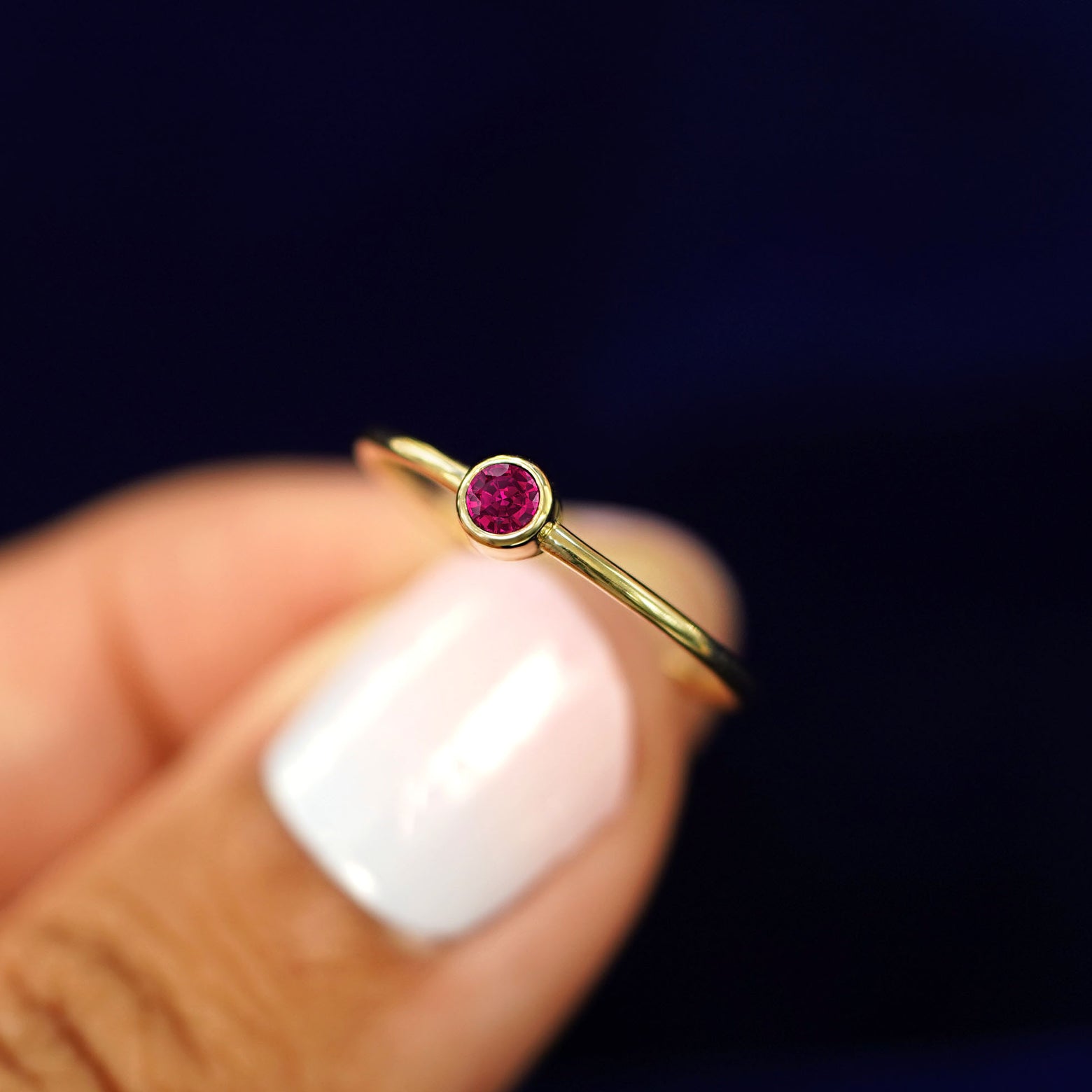 A model holding a 14k gold Ruby Ring between their fingers to show the details of the bezel set stone