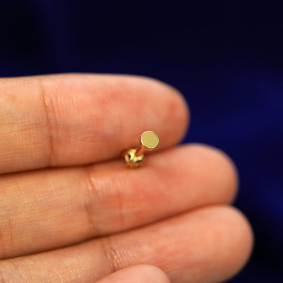 A solid gold Salt and Pepper Diamond Flatback Piercing laying facedown on a model's finger to show the end of the flat back