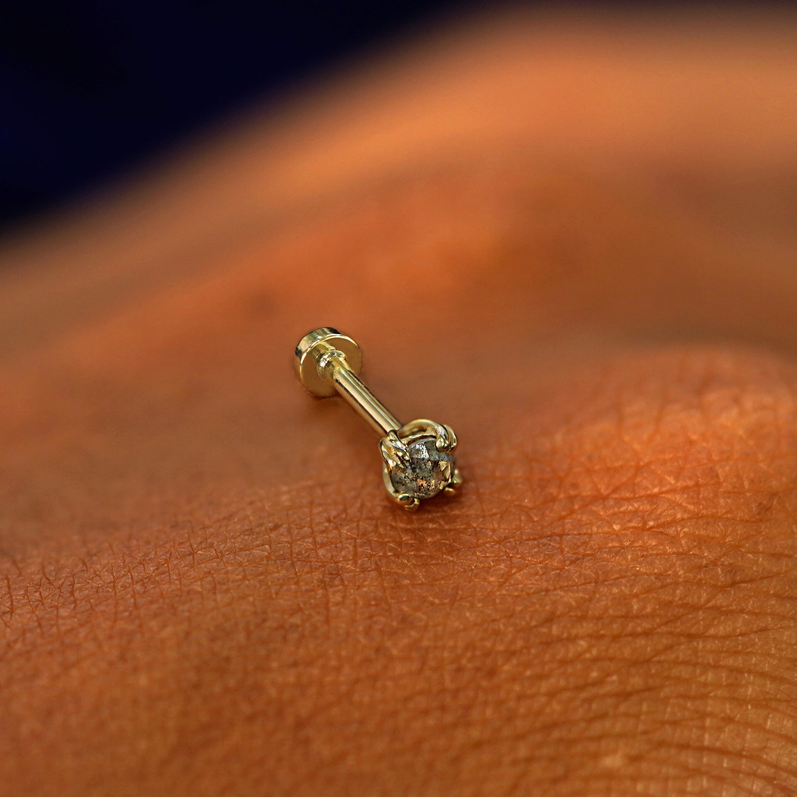 A solid 14k yellow gold Salt and Pepper Diamond Flatback Piercing resting on the back of a model's hand