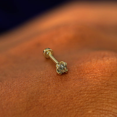 A solid 14k yellow gold Salt and Pepper Diamond Flatback Piercing resting on the back of a model's hand