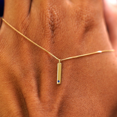 A solid gold sapphire Gemstone Bar Necklace resting on the back of a model's hand