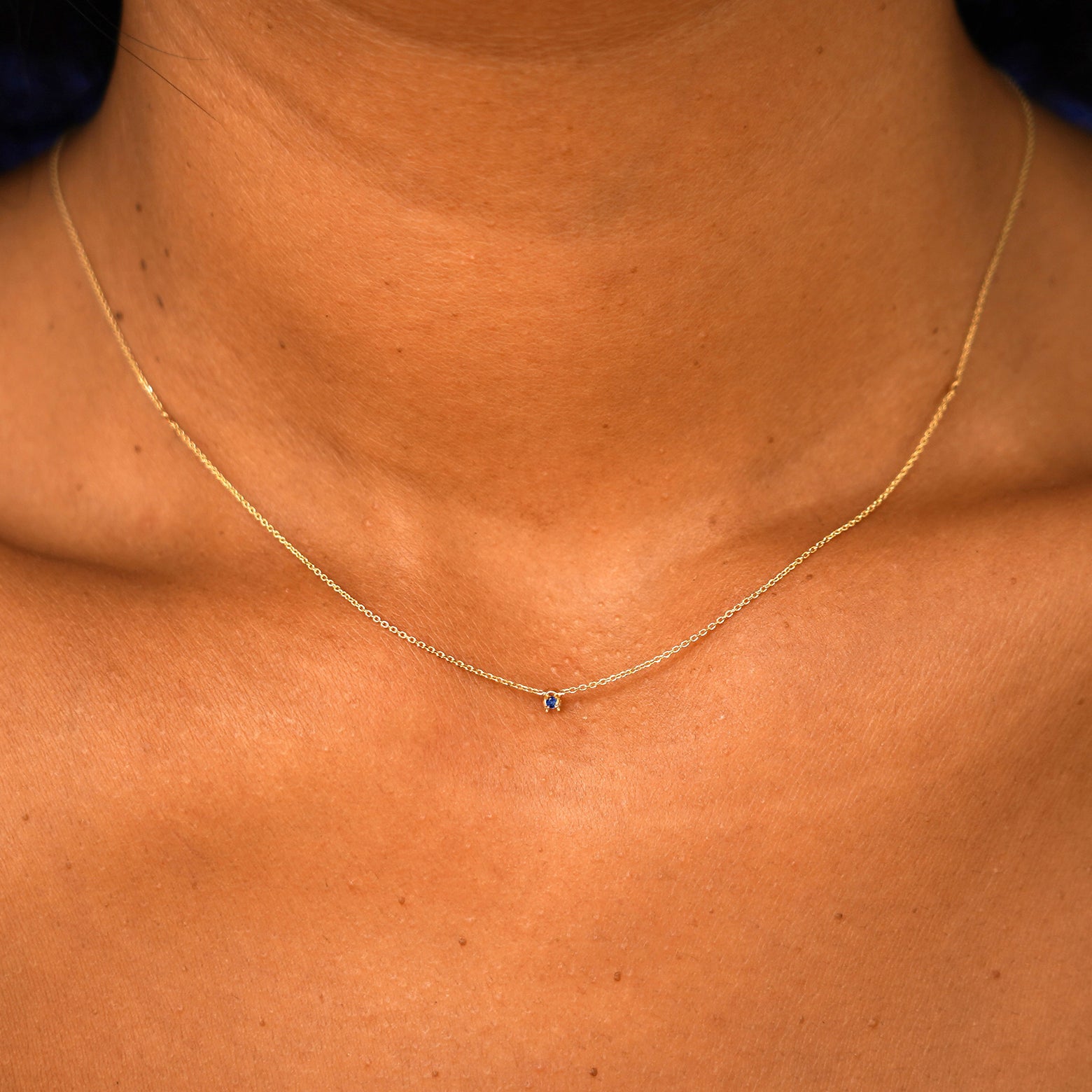 A model's neck wearing a solid 14k yellow gold Gemstone Cable Necklace in sapphire